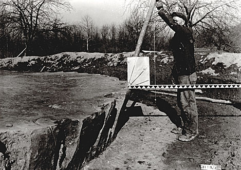 A WPA worker measures the angle of a wall post in the circular submound structure.