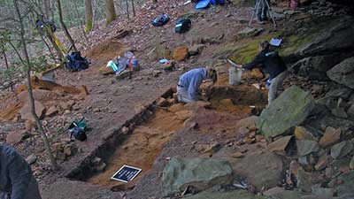 Archaeologists clean a trench for a photograph.