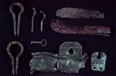Historic trade goods from the Bentley site - brass kettle fragments, an iron knife, an iron key, and iron/brass mouth harps.